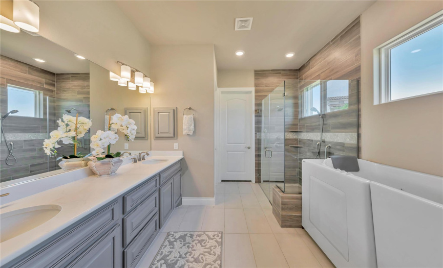 Double sinks and quartz counters add to the spa feel of the the primary bath. The door to the walk-in closet is located at rear of bathroom.