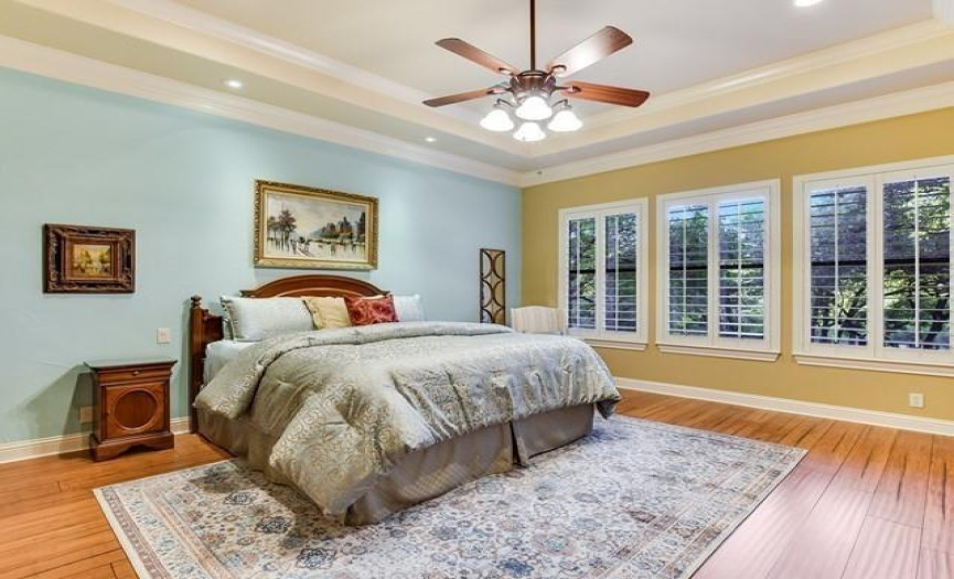 Enormous main-level master suite takes advantage of backyard views and exudes ease with wide planked bamboo floors, a coffered ceiling and custom plantation shutters. 